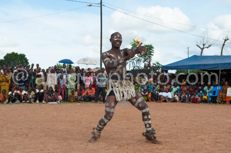 Africa photo — Un danseur traditionnel vêtu d’un costume orné de motifs blancs et noirs, tenant une branche feuillue, exécute une chorégraphie dynamiq