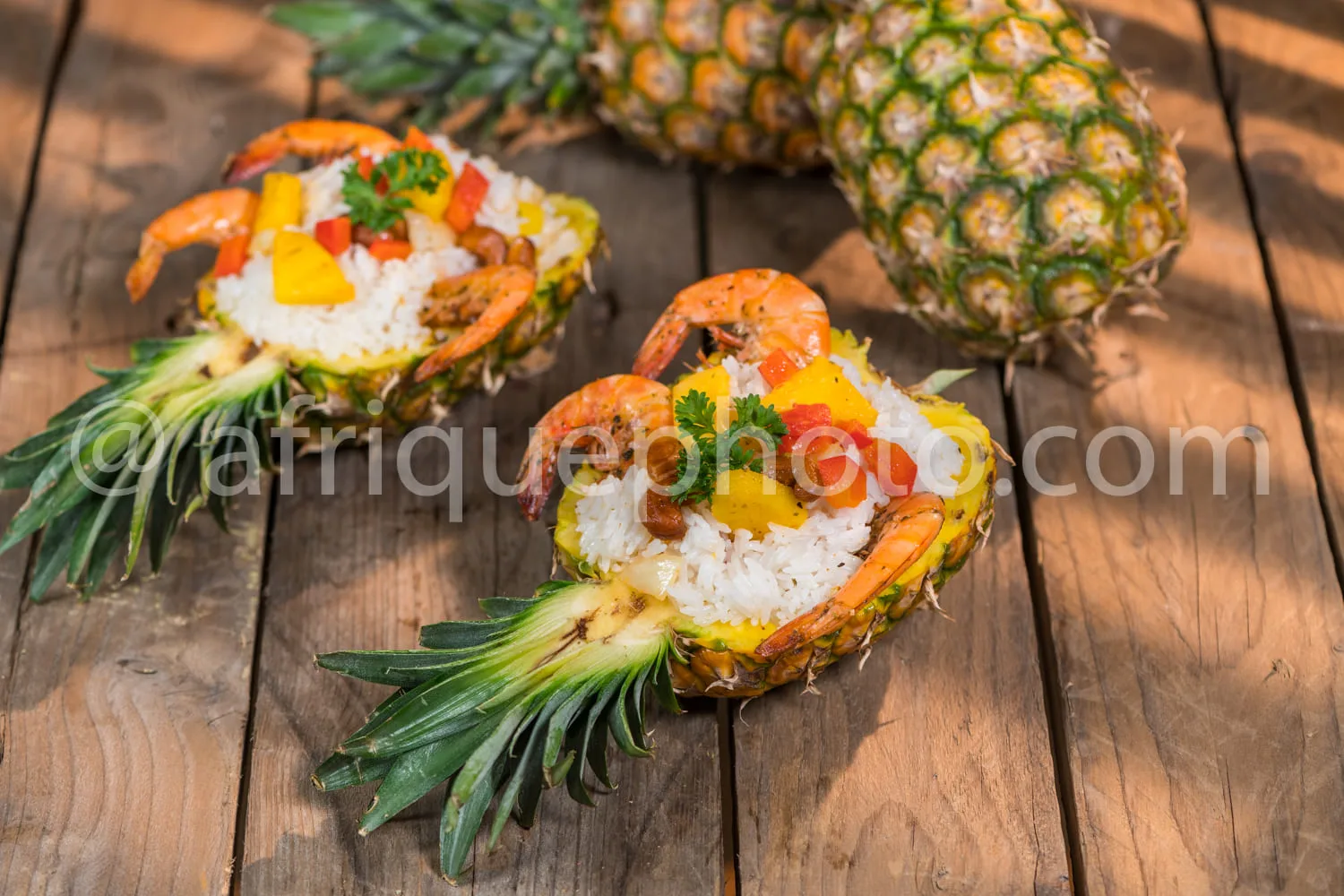 Africa photo — Deux demi-ananas ouverts contenant chacun un crabe garni de riz blanc, légumes colorés, fruits secs et herbes fraîches, posés sur une p