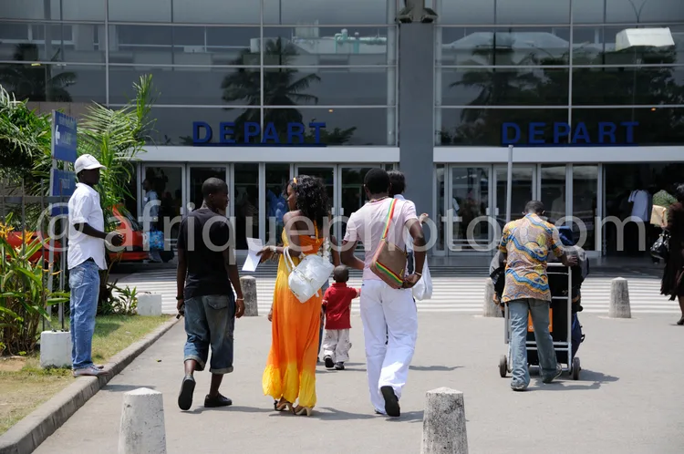 Africa photo — Un groupe de six personnes, dont une femme en robe orange vif et un homme en tenue blanche, marchent vers un bâtiment moderne avec des