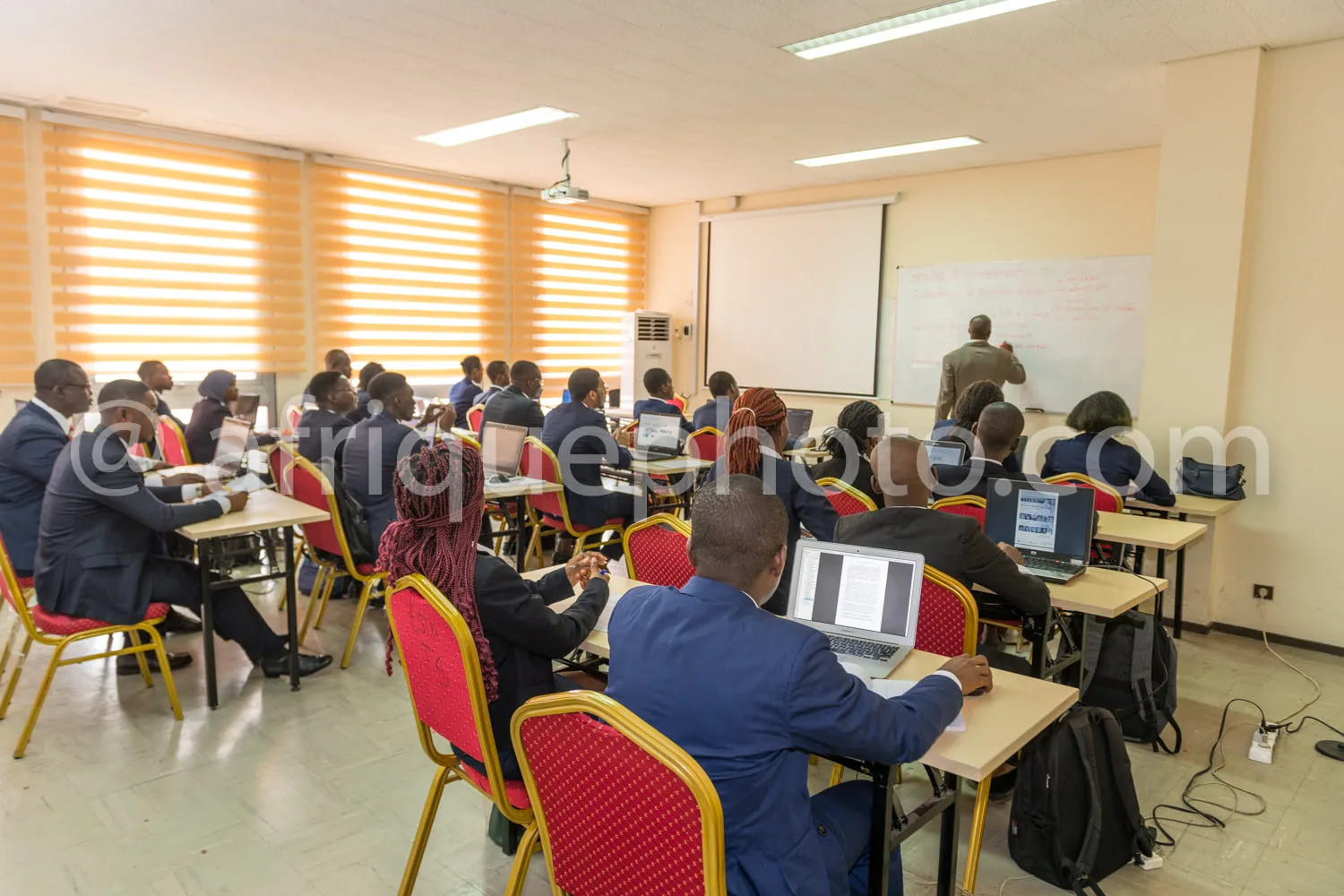 Africa photo — Une salle de formation où une vingtaine de participants, assis en rangées avec des chaises rouges, utilisent des ordinateurs portables.
