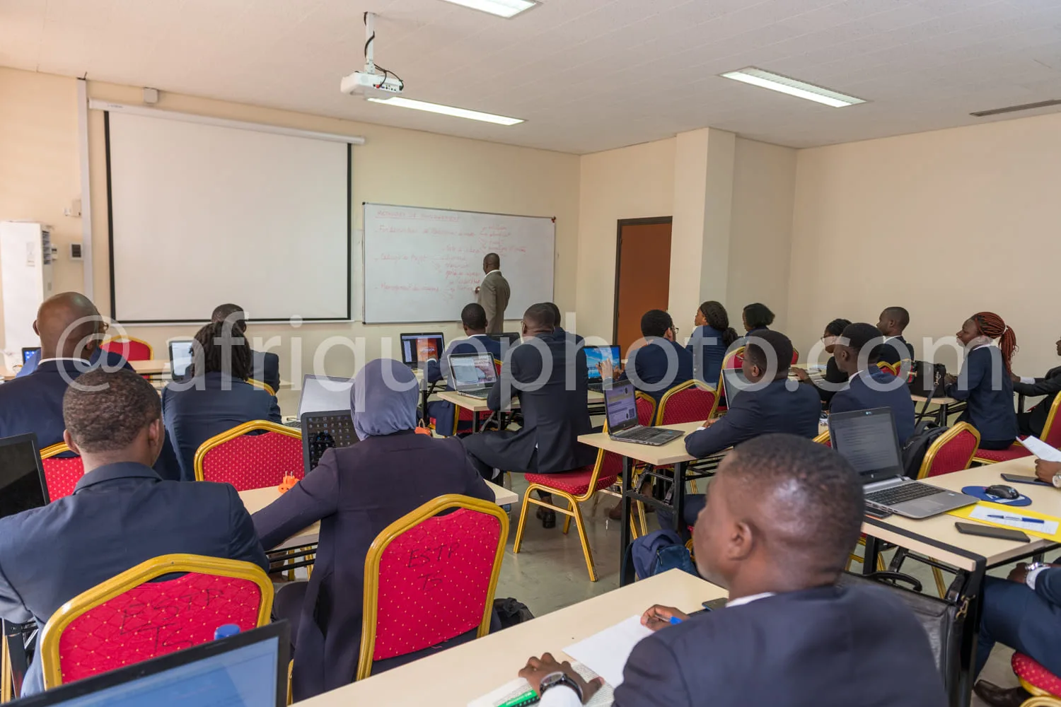 Africa photo — Une salle de formation professionnelle où une vingtaine de participants, assis sur des chaises rouges, suivent une présentation devant
