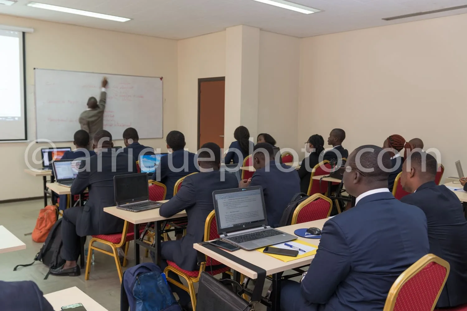 Africa photo — Une salle de formation où une vingtaine de participants, vêtus de costumes, travaillent sur des ordinateurs portables disposés sur des