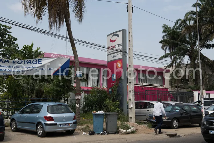 Africa photo — Image montrant le siège social de Microcred, un établissement bancaire, situé dans une rue bordée de palmiers. On aperçoit une façade r