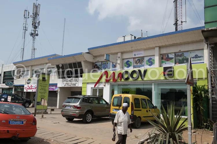 Africa photo — Un immeuble commercial avec une façade blanche et bleue abritant le bureau Latrille-Ena, des enseignes publicitaires et des commerces.