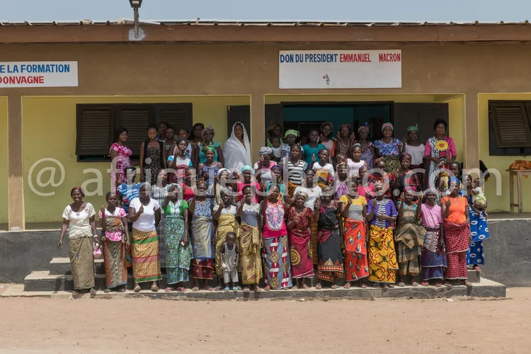 Africa photo — Un groupe de femmes souriantes, vêtues de tenues traditionnelles colorées, posent devant un bâtiment avec une pancarte indiquant 'Don d
