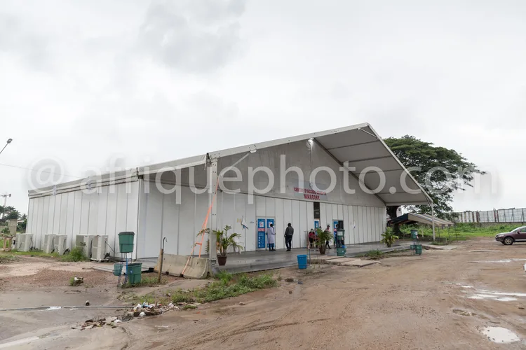 Africa photo — Une tente médicale blanche en extérieur, avec des panneaux d'information et des signalétiques sanitaires. Deux personnes en tenue de pr