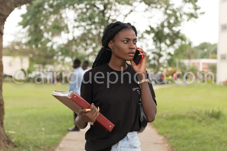 Africa photo — Une femme en vêtements professionnels, tenant un dossier rouge sous son bras gauche et parlant au téléphone portable de sa main droite,