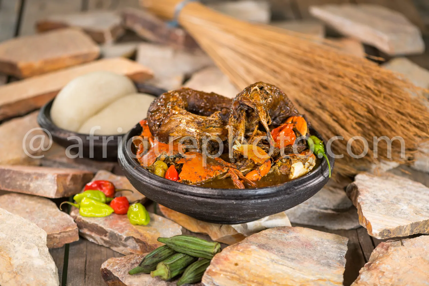 Africa photo — Un bol en terre cuite contenant un ragoût de crabe grillé, entouré de carottes cuites, de piments frais et de feuilles de courge, posé