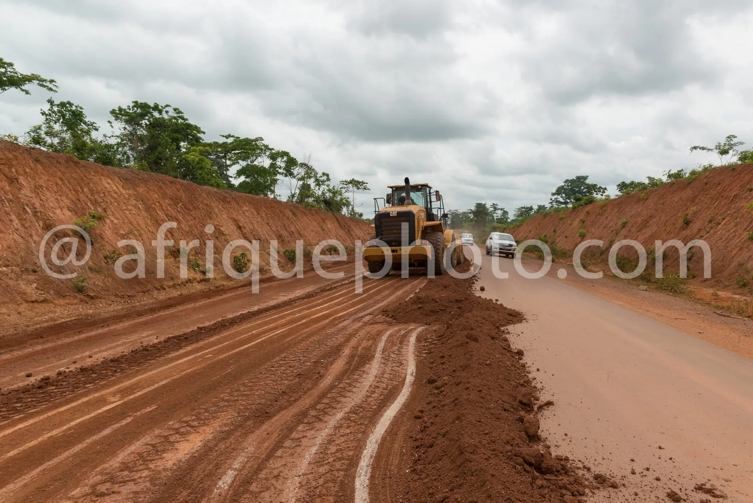 Africa photo — Une route en construction avec un engin jaune de terrassement en train de travailler sur la chaussée, un véhicule utilitaire derrière l