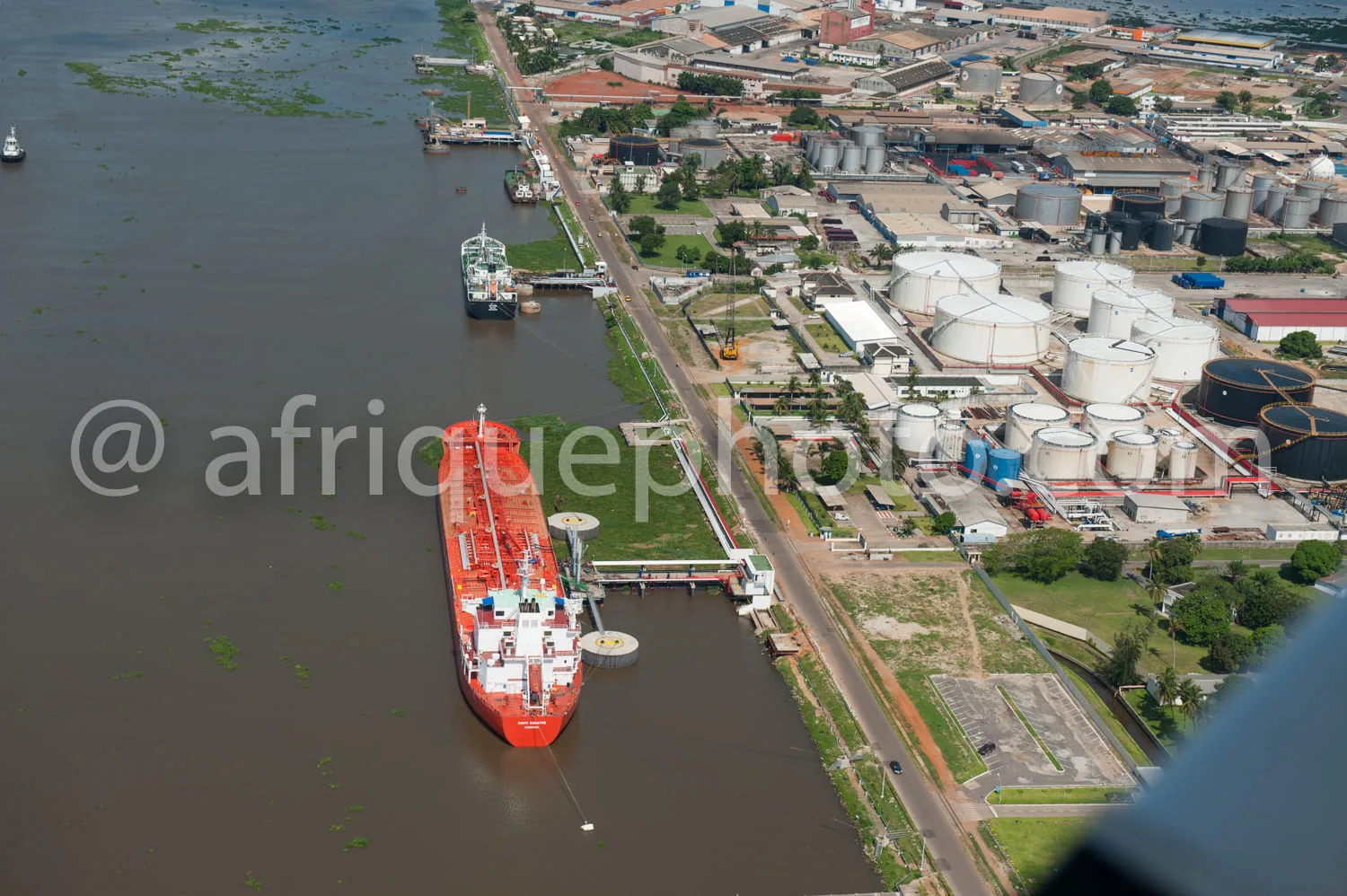 Africa photo — Vue aérienne d’un pétrolier rouge s’approchant d’un terminal portuaire équipé de nombreux réservoirs métalliques blancs, de bâtiments i