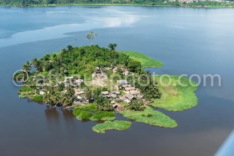 Africa photo — Une petite île verdoyante au milieu d'un grand plan d'eau, avec des maisons en bois et des palmiers, offrant une ambiance paisible et s