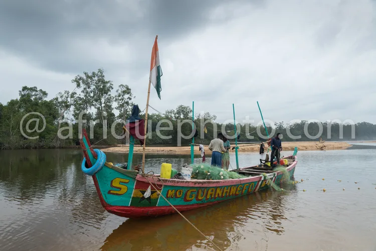Africa photo — Une pirogue colorée aux couleurs vives, arborant le drapeau du Mozambique, navigant sur un plan d’eau calme. Quatre pêcheurs sont visib