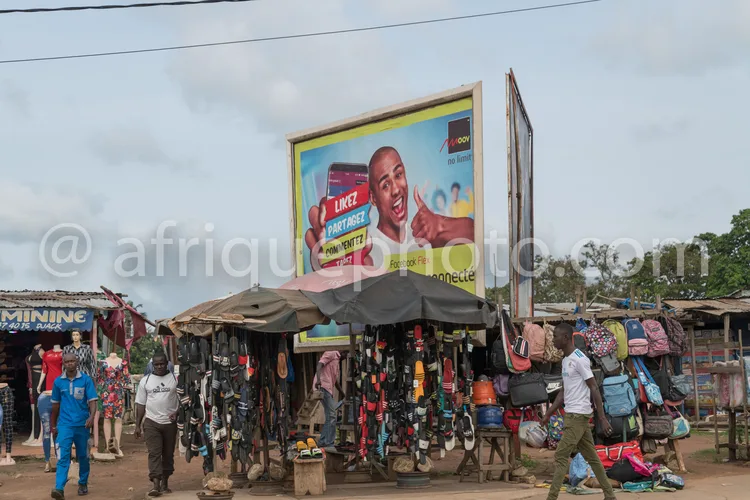 Africa photo — Une affiche publicitaire pour une marque de téléphone Lumée est visible en arrière-plan, avec un homme souriant tenant un smartphone. A