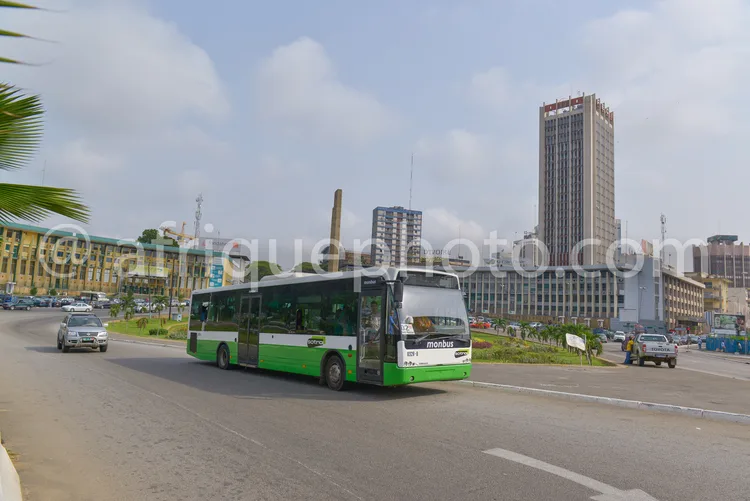 Africa photo — Un bus urbain moderne, vert et blanc, circule sur une route bien aménagée en ville, entouré d'immeubles de bureaux et d'un gratte-ciel