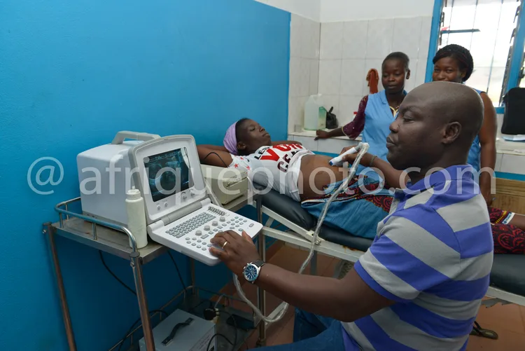 Africa photo — Un professionnel de santé effectue un examen échographique sur un patient allongé sur une table, avec un appareil portable branché. Une