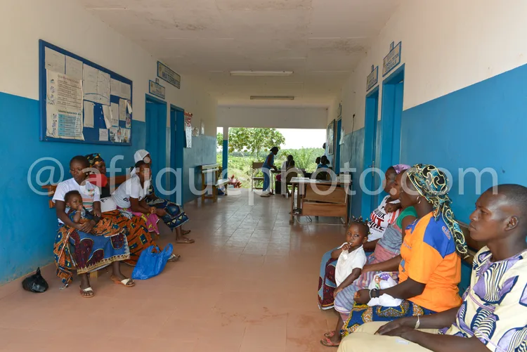 Africa photo — Une famille composée de quatre adultes et deux enfants est assise dans une salle d’attente médicale aux murs bleus. Les enfants sont su