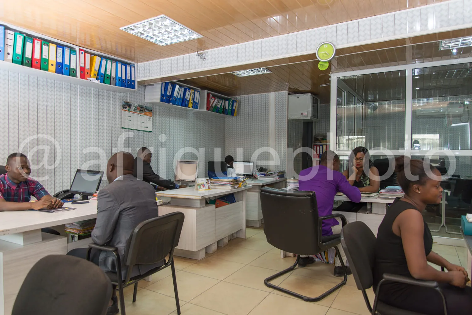 Africa photo — Une pièce lumineuse avec quatre personnes assises autour de tables de travail équipées d’ordinateurs et de dossiers. Des archives color