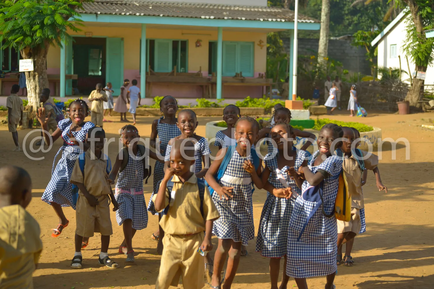 Africa photo — Un groupe d’enfants vêtus d’uniformes scolaires bleu et beige, souriant et courant joyeusement dans une cour de récréation en plein air