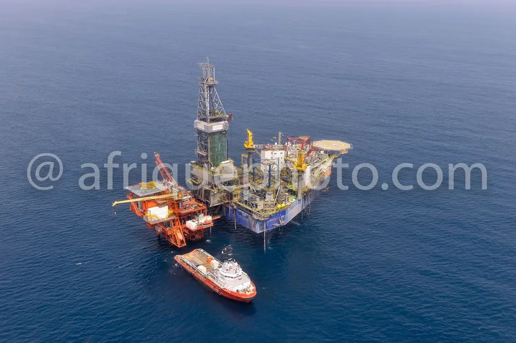 Africa photo — Vue aérienne d'une plateforme pétrolière offshore flottant sur une mer calme, entourée d'un bateau de soutien à sa droite. La structure