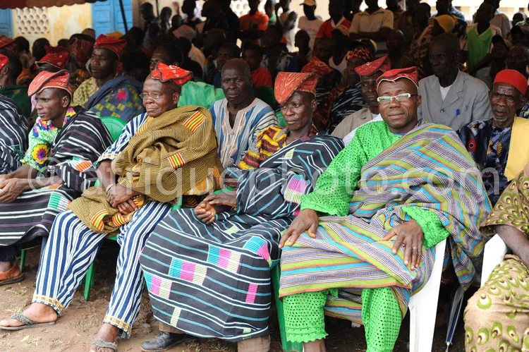 Africa photo — Assemblée de personnes assises sur des chaises en plastique, vêtues de boubous aux motifs géométriques variés et de turbans colorés, pa