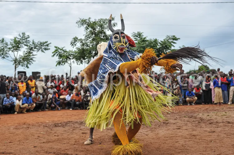 Africa photo — Un danseur vêtu d’un costume traditionnel africain richement décoré, portant un masque à cornes et des plumes, en pleine performance de