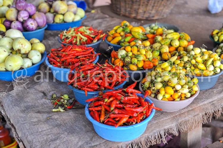 Africa photo — Image d’un étalage de marché traditionnel avec des bols bleus contenant des piments rouges entiers et coupés, des poivrons jaunes et ve