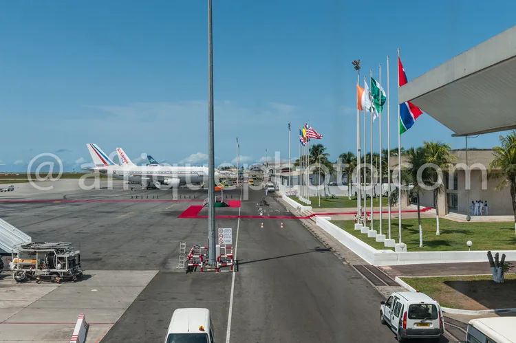 Africa photo — Un avion Air France blanc et bleu se déplace sur une piste d'aéroport, entouré de véhicules de service. À droite, une rangée de drapeau