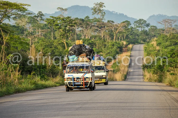 Africa photo — Deux véhicules légers roulant sur une route asphaltée en pleine forêt tropicale. Le premier est surchargé de passagers assis sur le toi