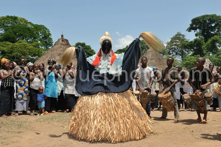 Africa photo — Un danseur vêtu d'un costume traditionnel africain, masqué et debout sur une structure en paille, exécute une danse devant un public at