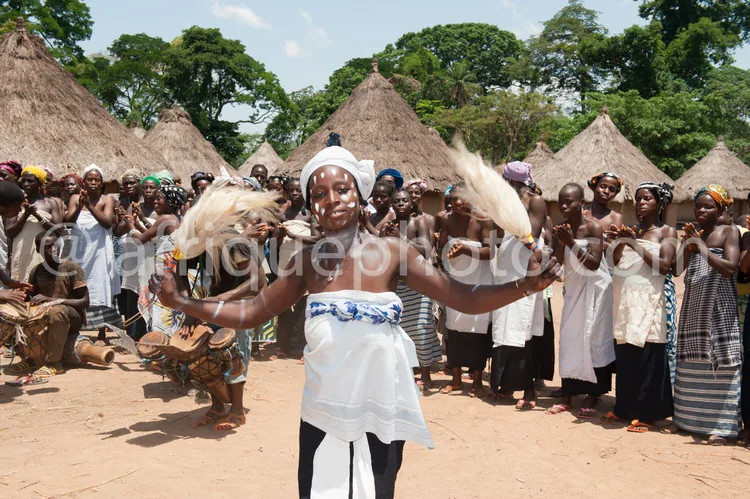 Africa photo — Une femme au centre, vêtue d'une tenue blanche et d'un voile, danse les bras levés en agitant des plumes blanches, entourée d'un groupe