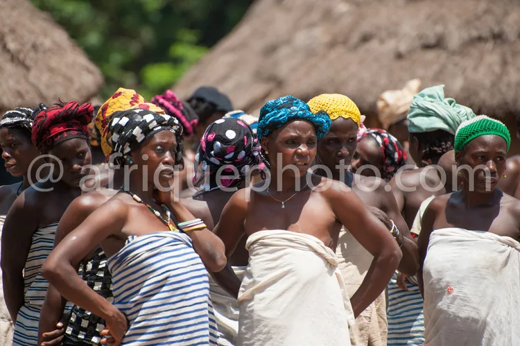 Africa photo — Un groupe de femmes en mouvement, vêtues de pagnes aux motifs variés et portant des coiffes colorées, participant à une danse tradition
