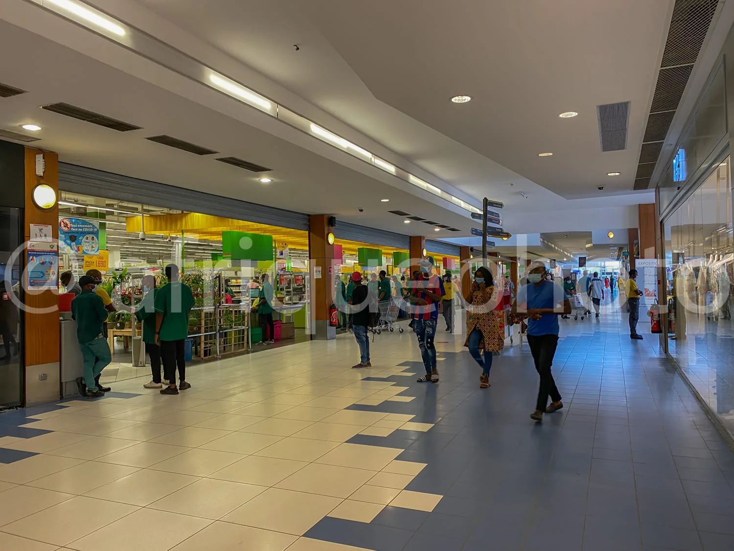 Africa photo — Intérieur d’un supermarché lumineux avec des clients en train de faire leurs courses, certains portant des masques. Les rayons sont bie