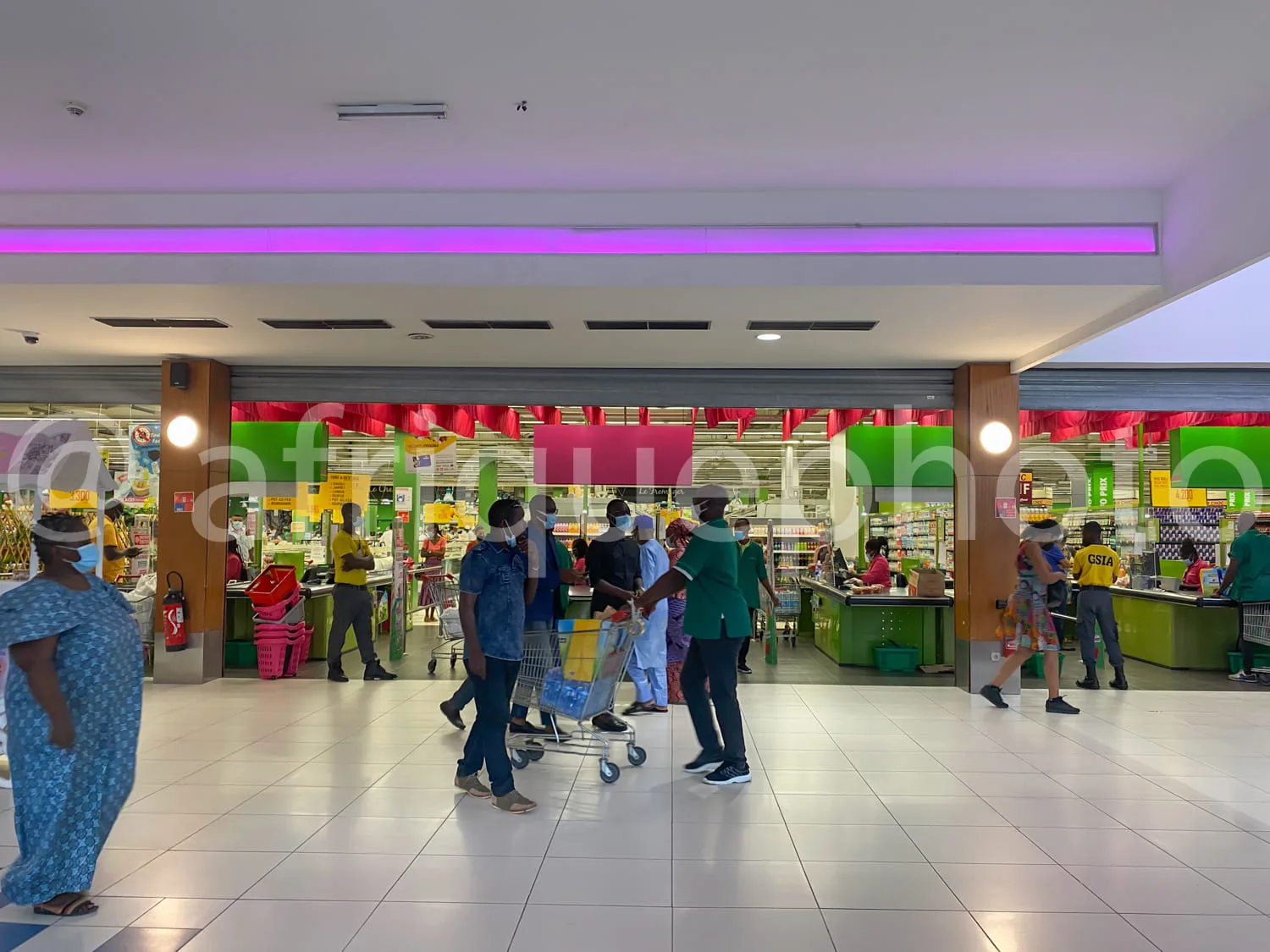 Africa photo — Intérieur lumineux d’un supermarché avec plusieurs clients en mouvement. Certains poussent des chariots, d’autres marchent vers les ray
