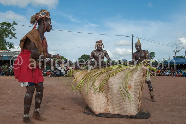 Africa photo — Trois hommes vêtus de costumes traditionnels africains colorés, dont deux portent des coiffures ornées et des peintures corporelles, ex