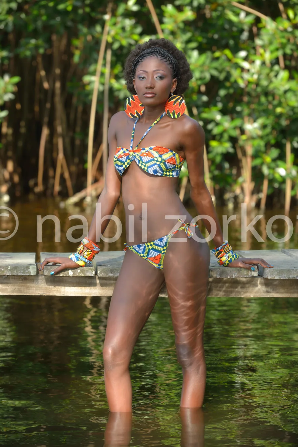 Africa photo — Une femme debout sur une bordure de pierre au bord d'une eau calme, vêtue d'un maillot de bain deux-pièces aux motifs géométriques bleu