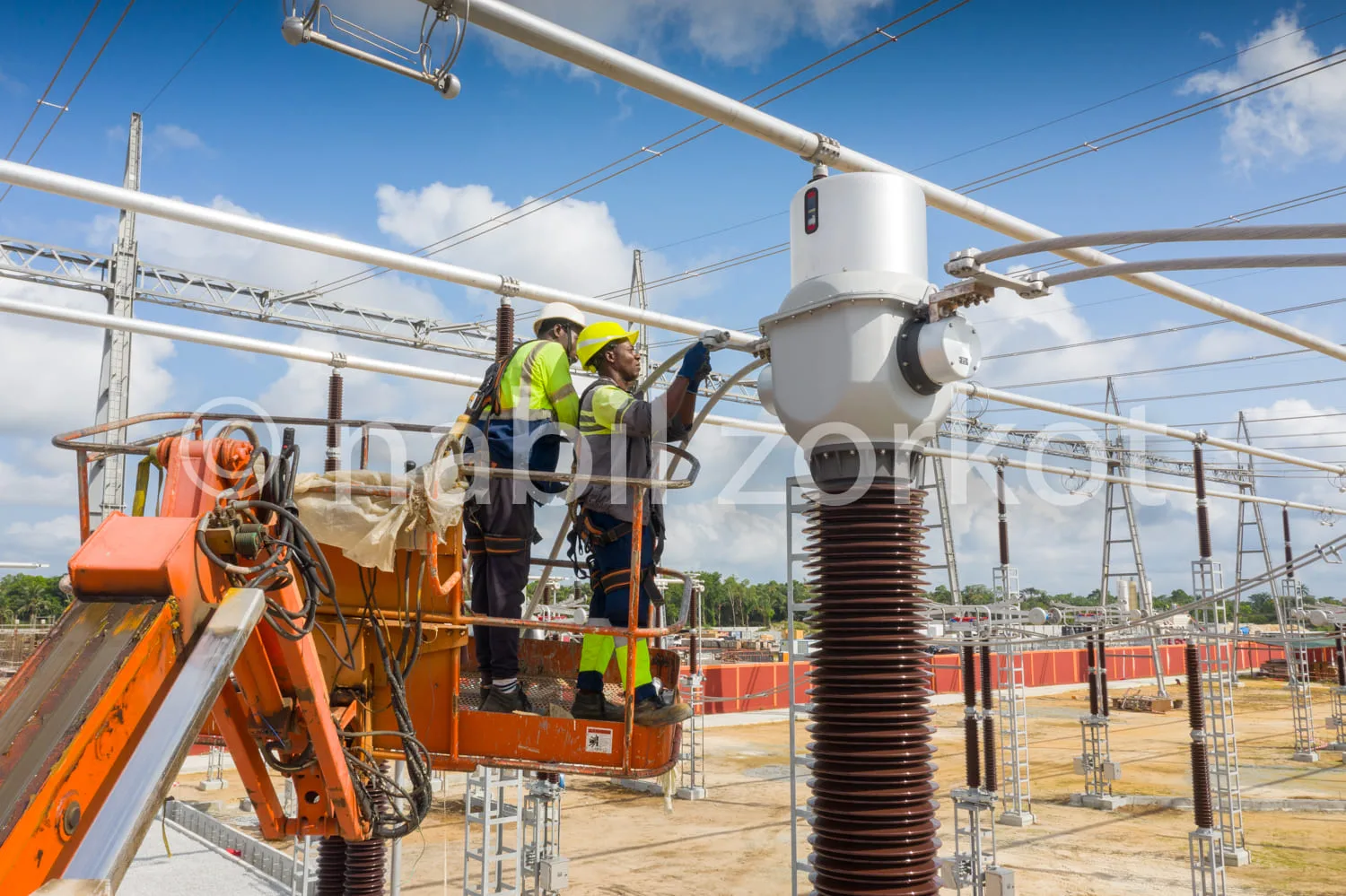 Africa photo — Deux techniciens équipés de casques jaunes et de combinaisons de sécurité travaillent sur un poste électrique haute tension. Ils sont p