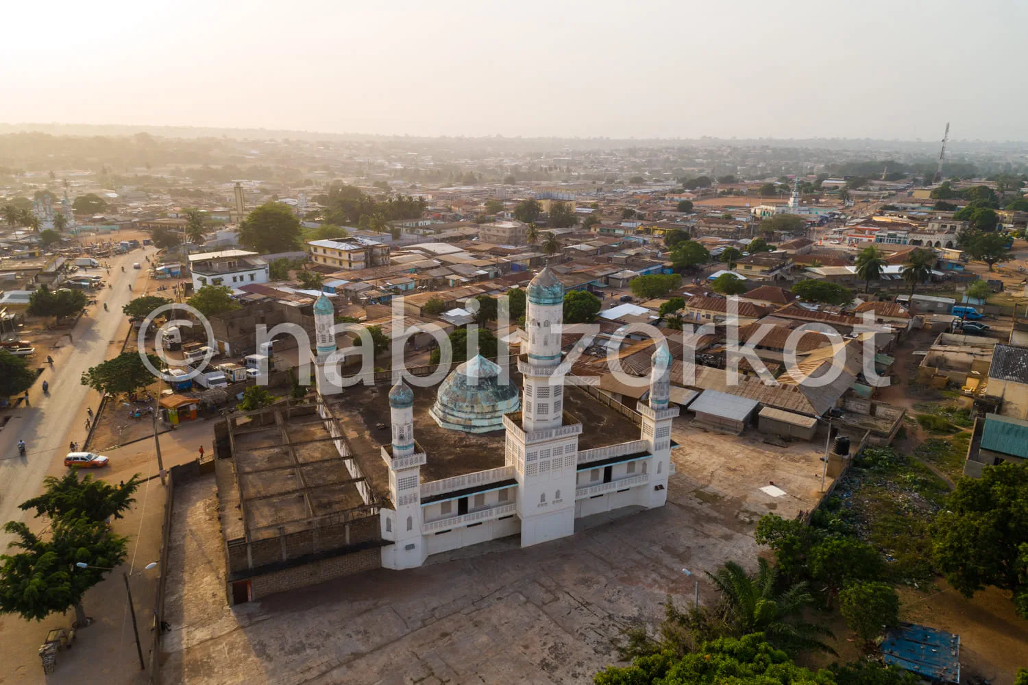 Africa photo — Vue aérienne d'une grande mosquée blanche avec deux minarets et un dôme bleu turquoise, entourée de bâtiments et de rues animées dans u