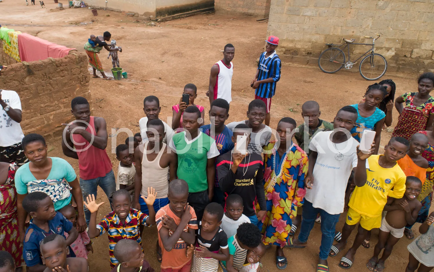 Africa photo — Un groupe d’une vingtaine d’enfants et adolescents souriants, posant devant un bâtiment en terre battue dans un cadre rural. Certains p