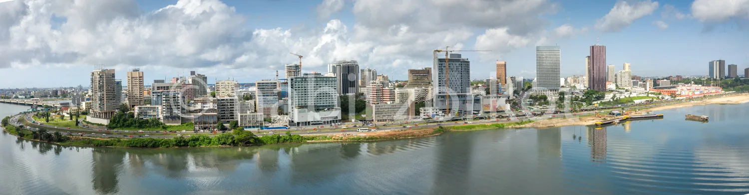 Africa photo — Une vue panoramique d'une ville dynamique bordée par un large fleuve calme, avec des gratte-ciels modernes, des bâtiments en constructi