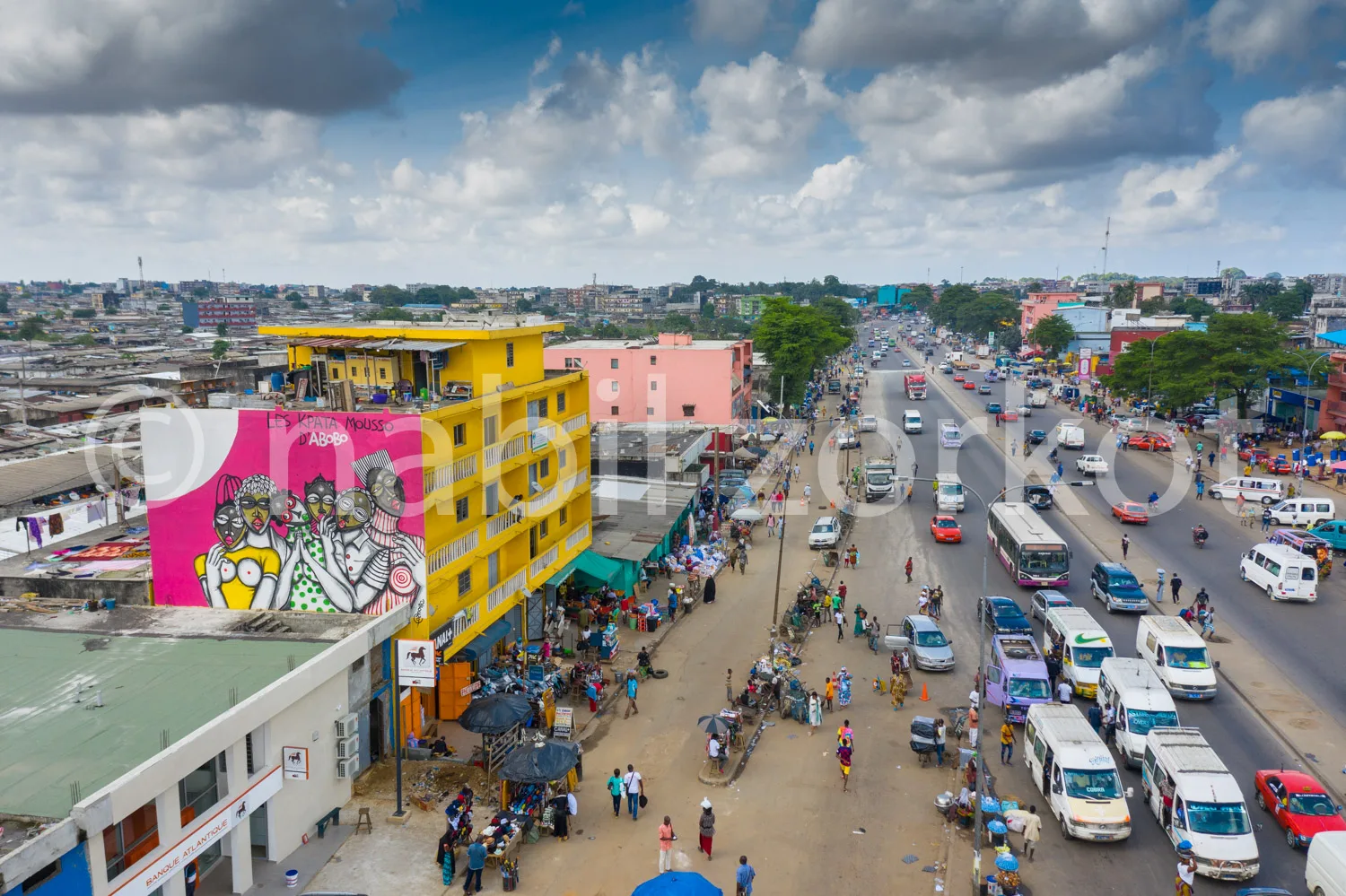 Africa photo — Vue aérienne d'une rue africaine très fréquentée avec un immeuble jaune orné d'une fresque murale colorée représentant des personnages