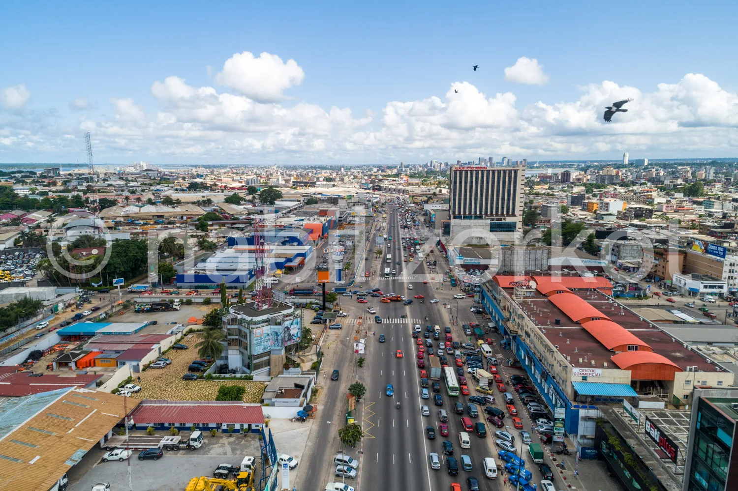 Africa photo — Une vue aérienne d'une ville africaine montrant une large avenue très fréquentée avec des véhicules en mouvement, des bâtiments colorés