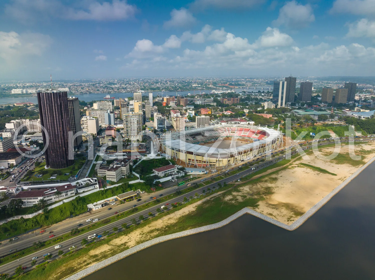 Africa photo — Image aérienne montrant un stade de grande capacité entouré de bâtiments urbains, une route bordée de voitures, une plage de sable et u