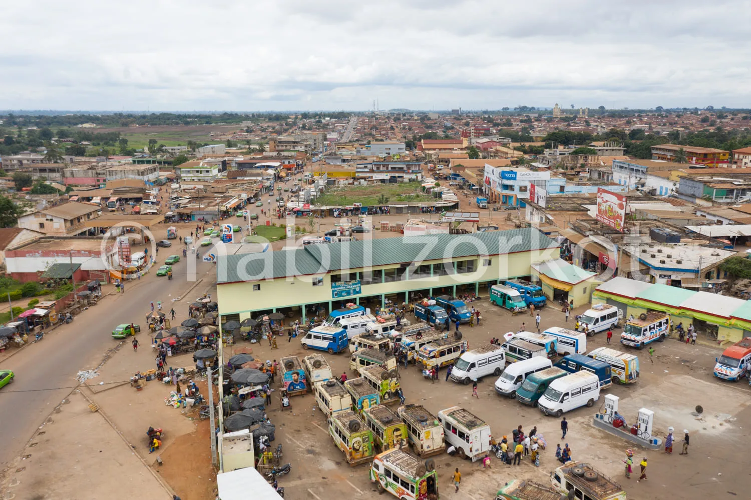 Africa photo — Vue aérienne d’une gare routière très fréquentée en Afrique, avec de nombreux minibus colorés stationnés sous une grande structure couv