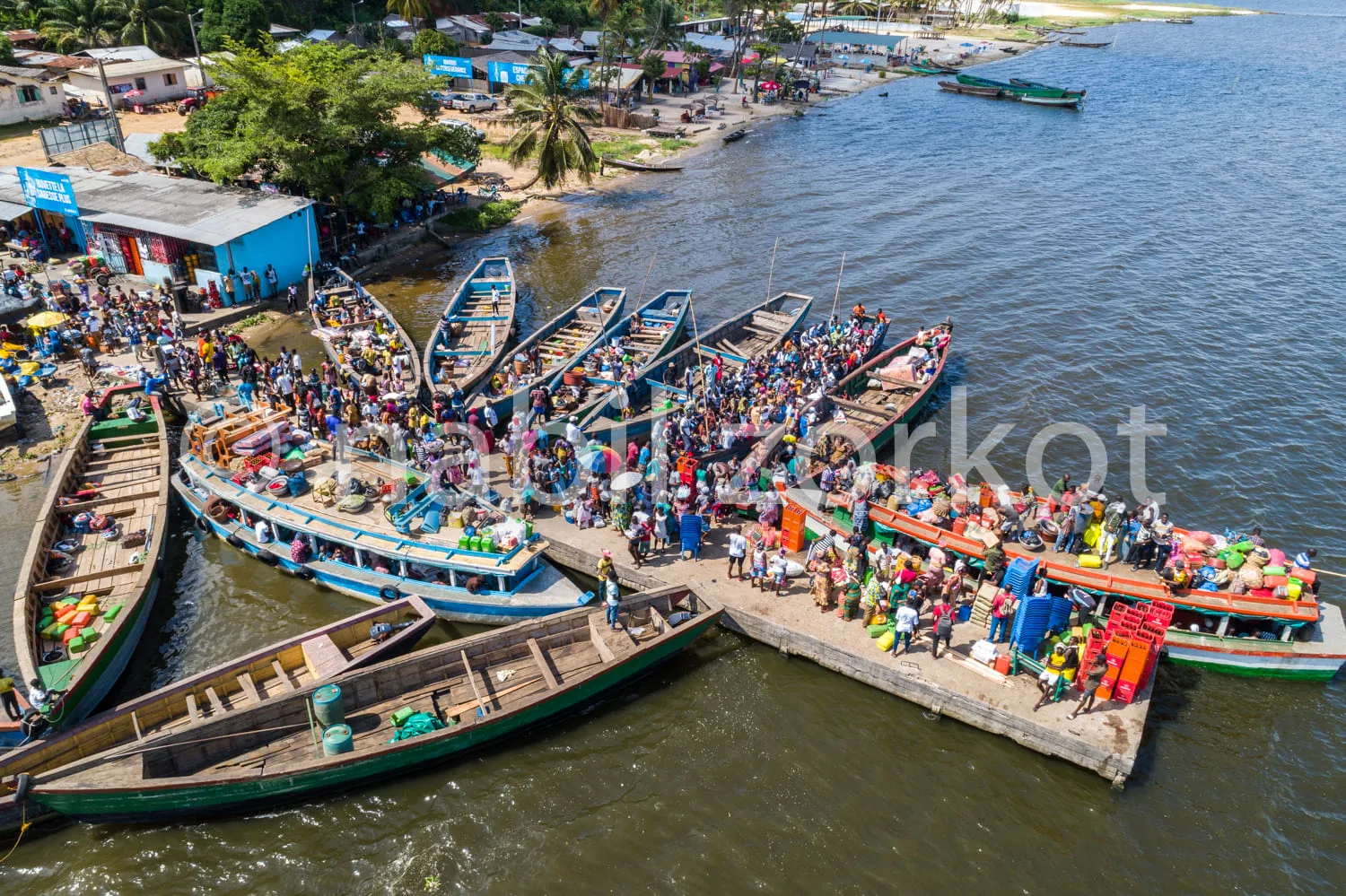 Africa photo — Vue aérienne d’un port où plusieurs bateaux en bois, remplis de passagers, sont amarrés à une jetée en béton. On entend des rires et de