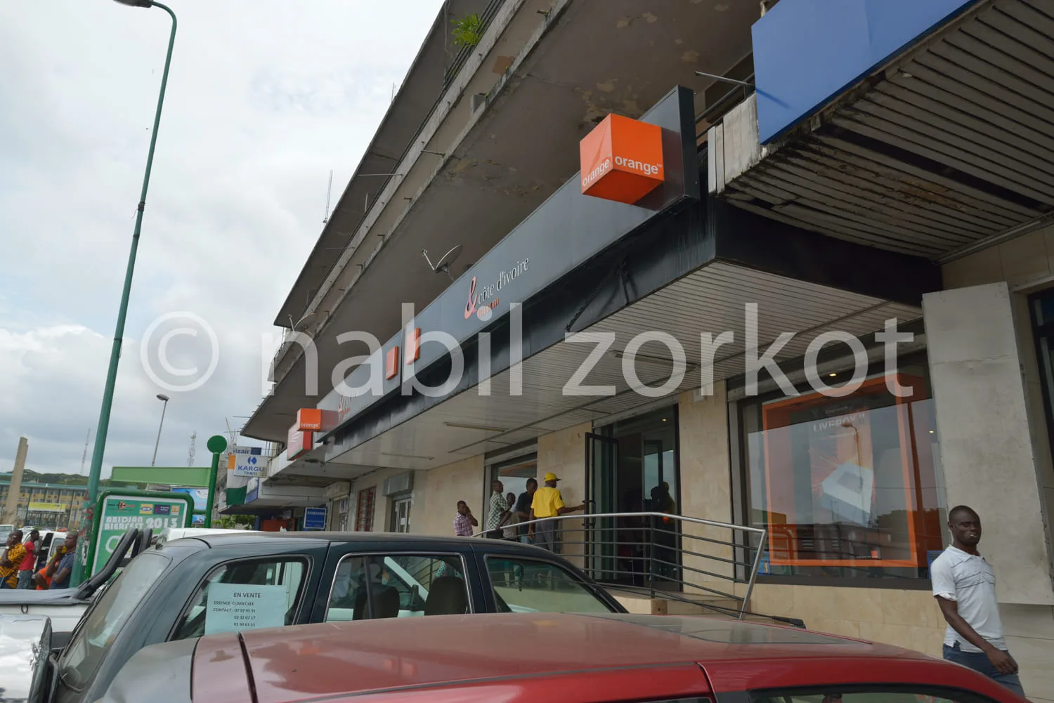 Africa photo — Photo d’une boutique Orange située en rez-de-chaussée d’un bâtiment commercial, avec une enseigne orange accrochée en saillie, une vitr