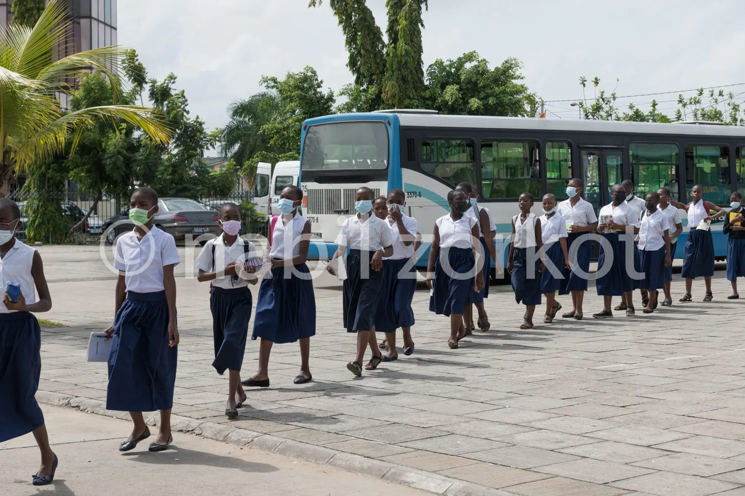 Africa photo — Un groupe d'élèves vêtus d'uniformes scolaires blancs et bleus, portant des masques, marchent en file indienne vers un bus scolaire bla