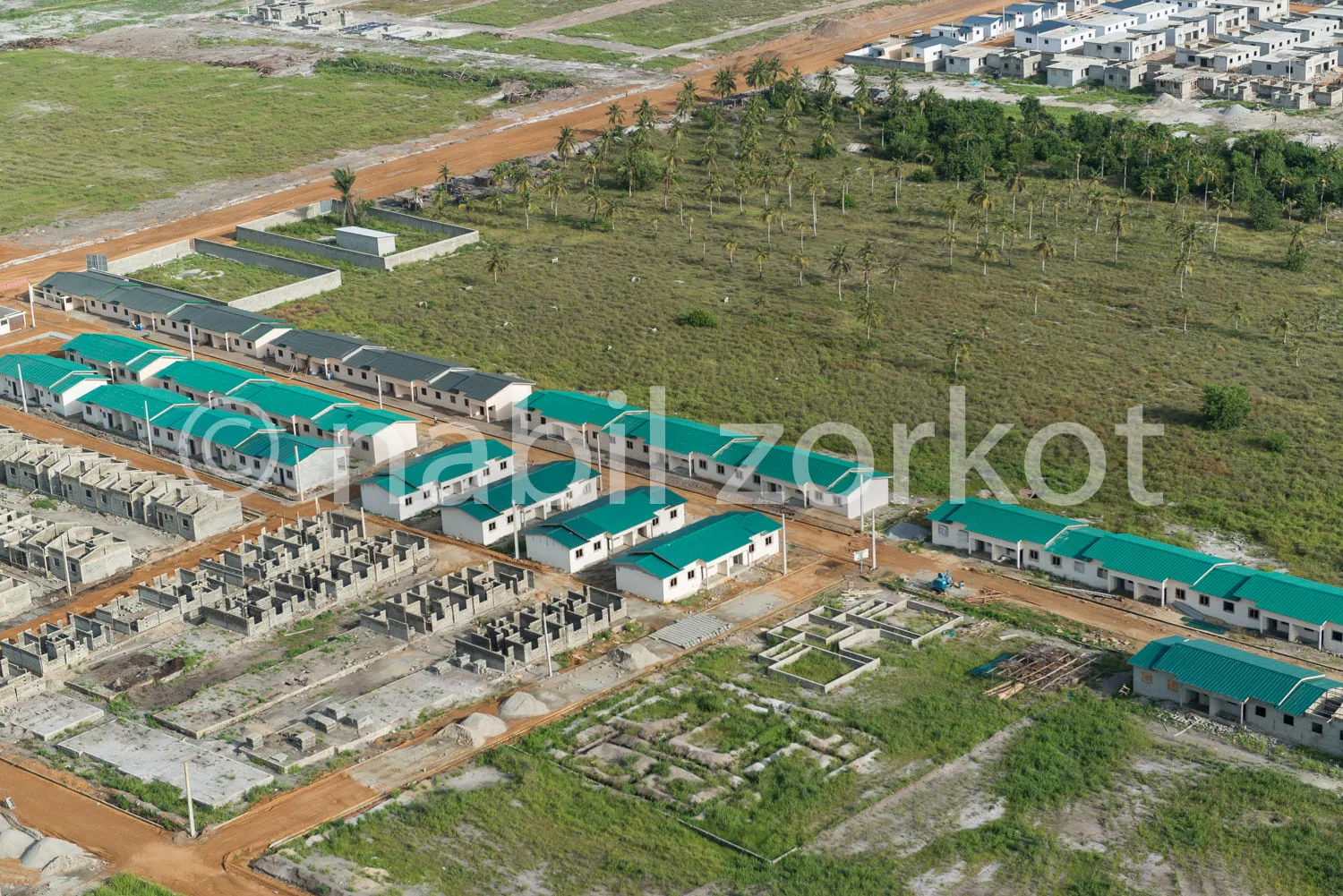 Africa photo — Vue aérienne d’un lotissement en construction avec des rangées de maisons individuelles aux toits verts, entourées de terrains en cours