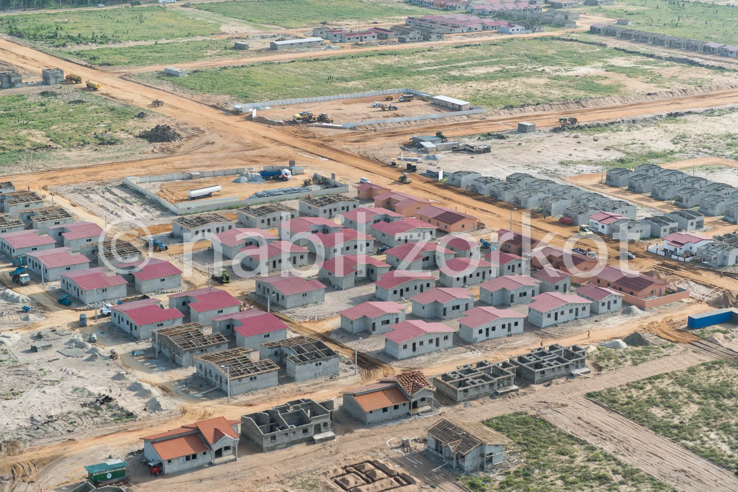 Africa photo — Image montrant une vaste zone de construction avec des maisons en cours de finalisation, des routes en terre et des espaces verts autou