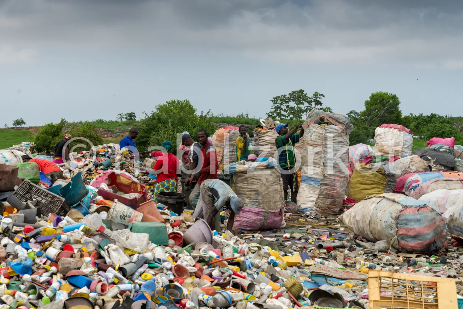 Africa photo — Groupe de personnes triant et collectant des déchets plastiques et divers matériaux dans une décharge à ciel ouvert, avec des sacs remp