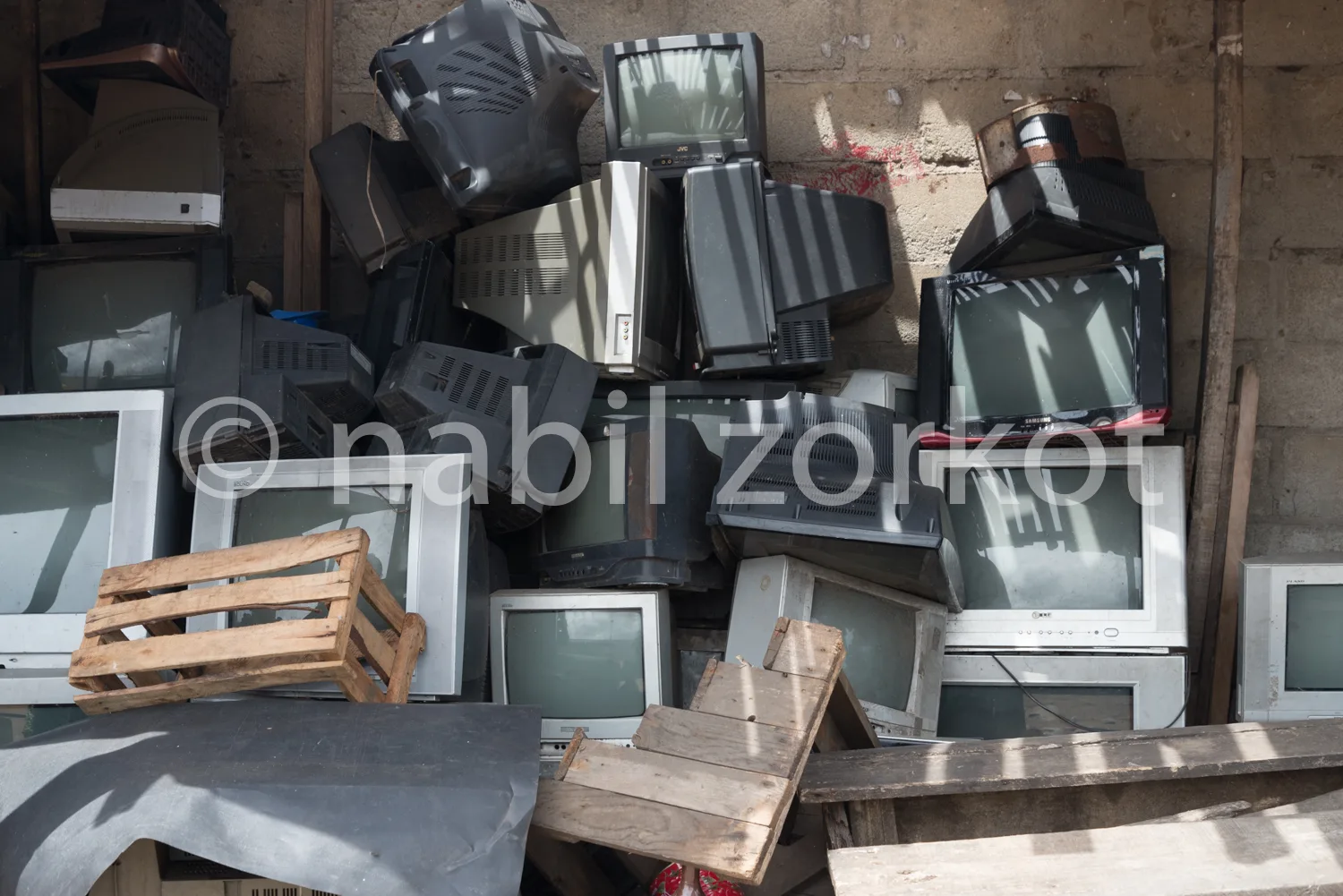 Africa photo — Un amas de téléviseurs anciens de différentes tailles et marques, certains posés à l’envers, entourés de meubles en bois abîmés et de c